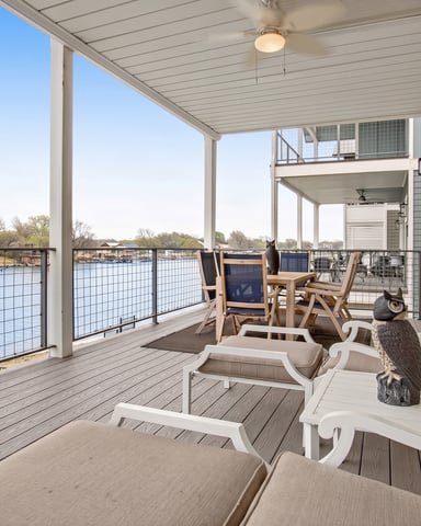 Waterfront lawn with Adirondack chairs around fire pit, dock with covered pavilion, and river view with distant houses and forested hills