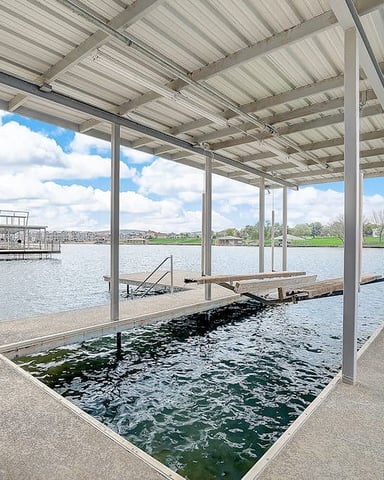 Waterfront lawn with Adirondack chairs around fire pit, dock with canopy, and river view with forested hills