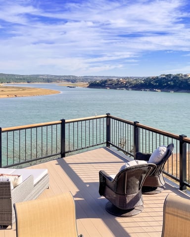 Waterfront lawn with Adirondack chairs around fire pit, dock with covered pavilion, and river view with forested hills.
