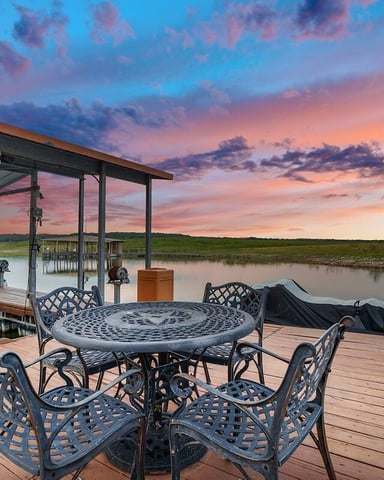 Covered deck with wicker seating, wooden railings, and expansive views of rolling hills and blue sky with clouds