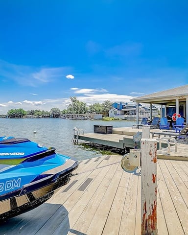 Covered waterfront deck with lounge chairs, grill, and ceiling fan overlooking lake and trees